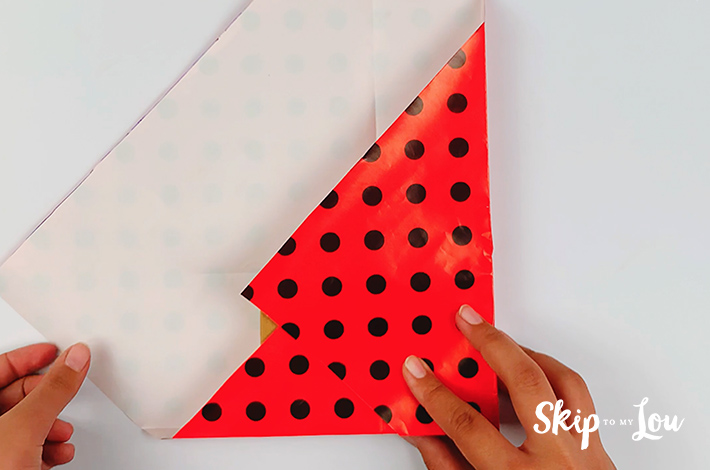 Two hands folding the right hand side of the paper over the box, making a clean edge along the side of the box.