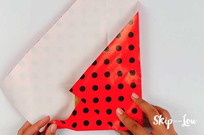 Two hands starting to fold the left hand side of the paper over the box.