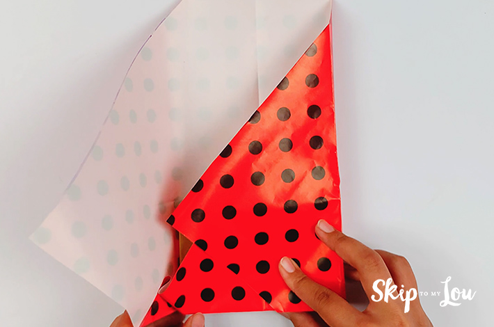 Two hands folding the left hand side of the paper over the box, making a clean edge along the side of the box.