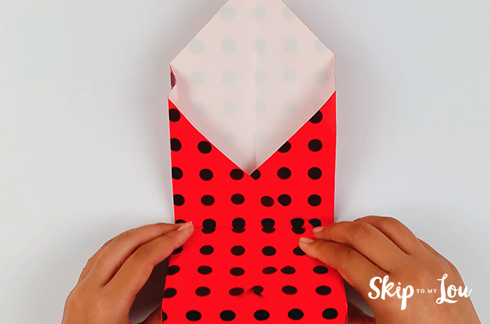 Two hands folding the already wrapped section of the box upwards.