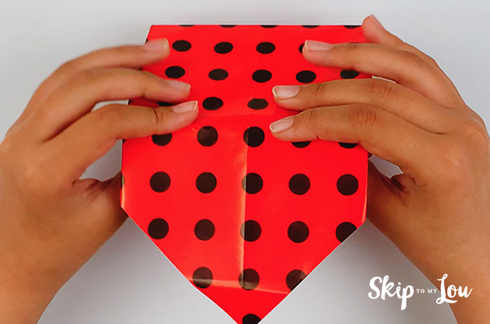 Two hands flipping the gift box over to start tucking in the top flap.