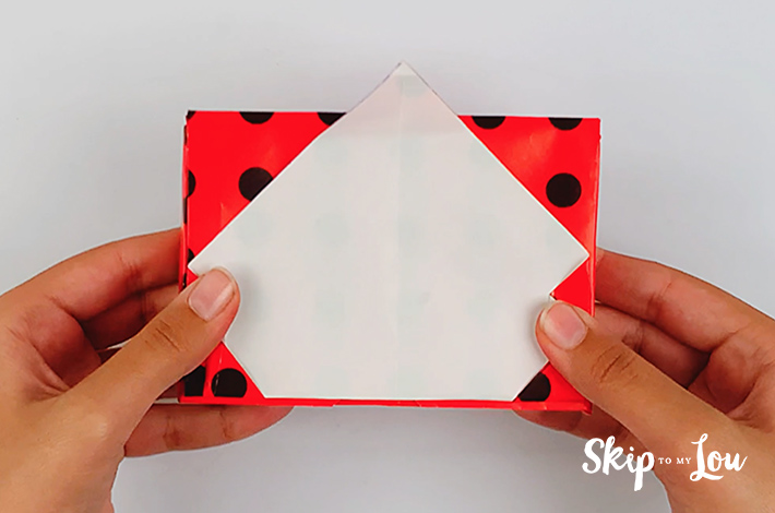 Two hands flipping the top flap of the wrapping paper back over the gift box.