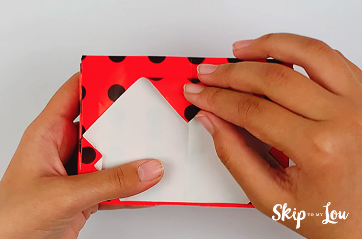 Two hands folding the top triangle of flap of the wrapping paper back over.