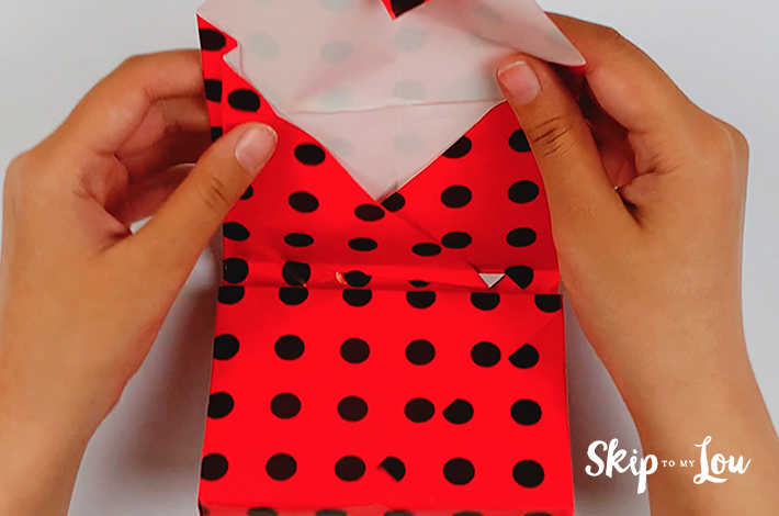 Two hands folding the top flap back over the gift box.