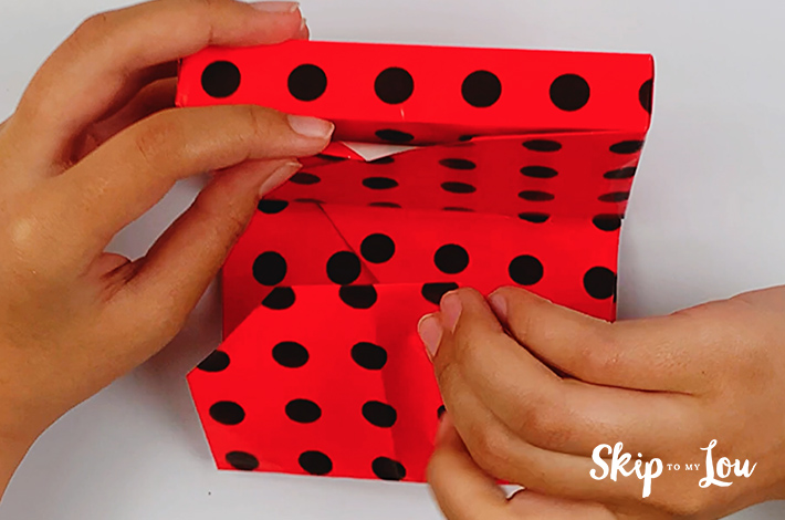Two hands folding the top flap of the wrapping paper inwards.