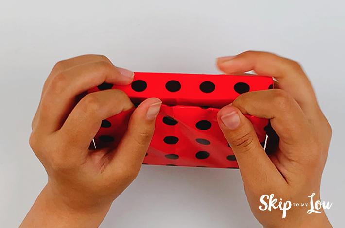 Two hands flattening the seams once the wrapping paper has been tucked in.