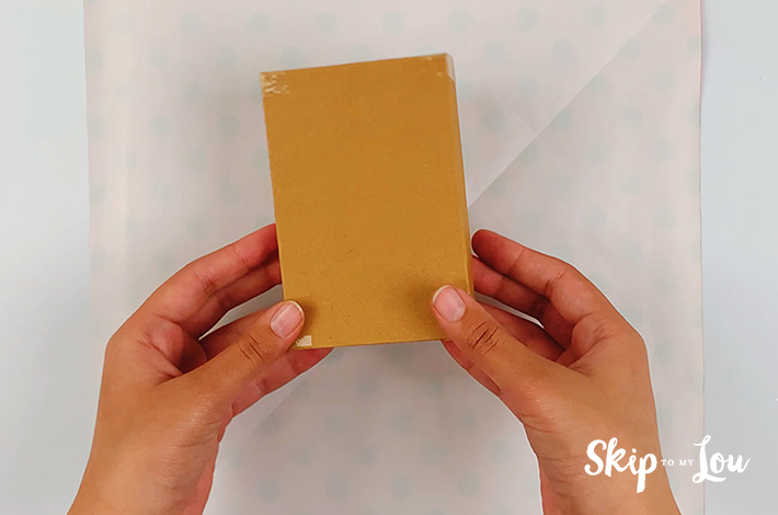 Two hands holding a gift box over the piece of wrapping paper.