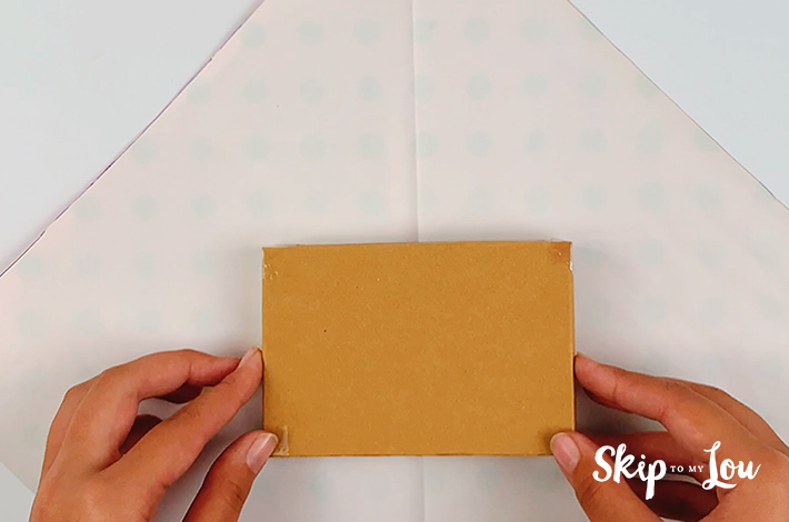 Two hands placing the gift box in the center of the paper.