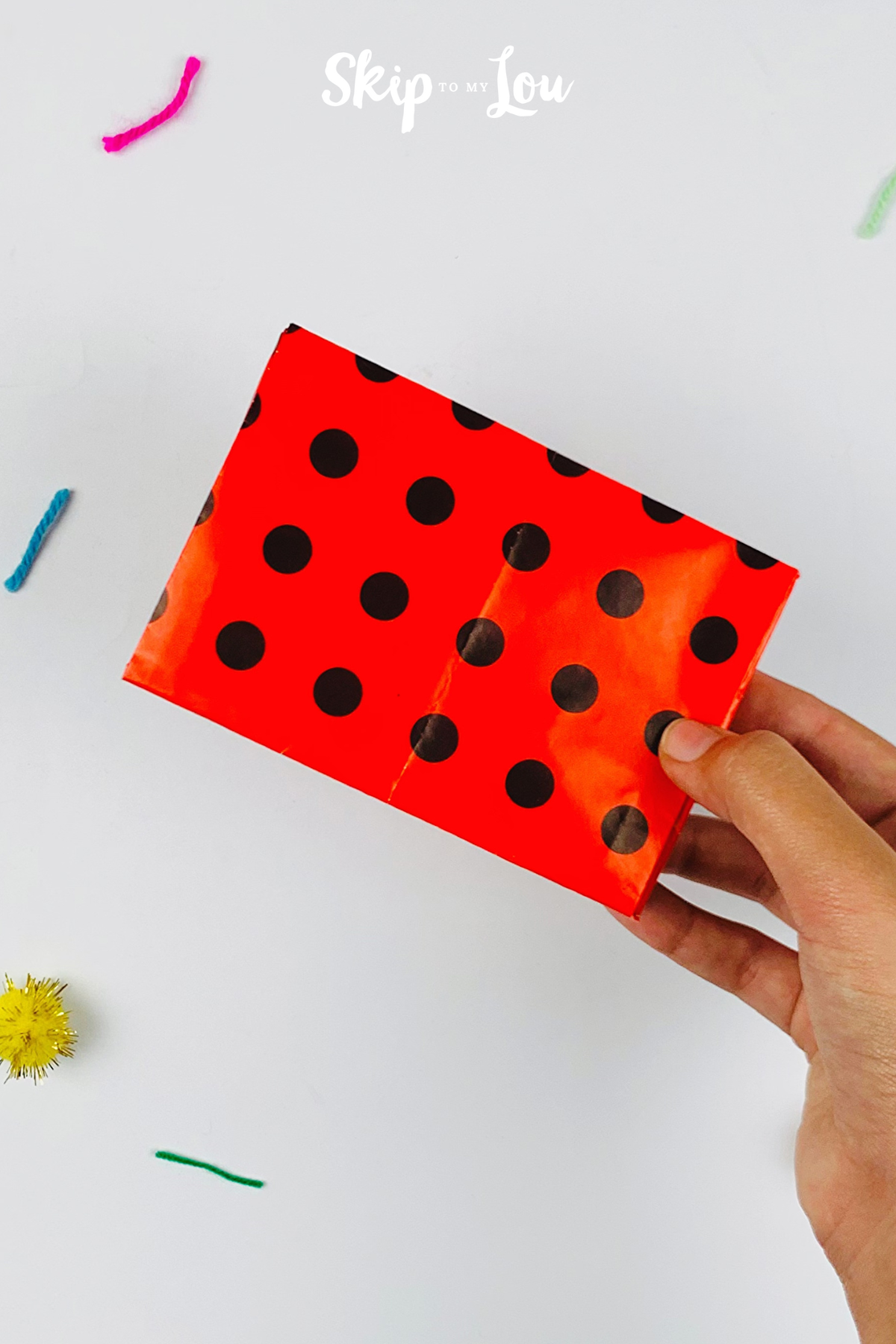 Two hands holding up a gift wrapped in using the Skip to My Lou method.