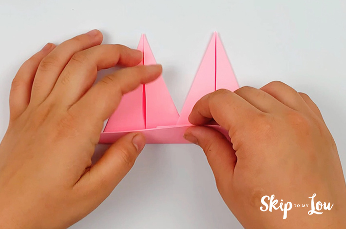 Two hands securing the two spikes by folding the bottom of the paper upwards again to its original fold.