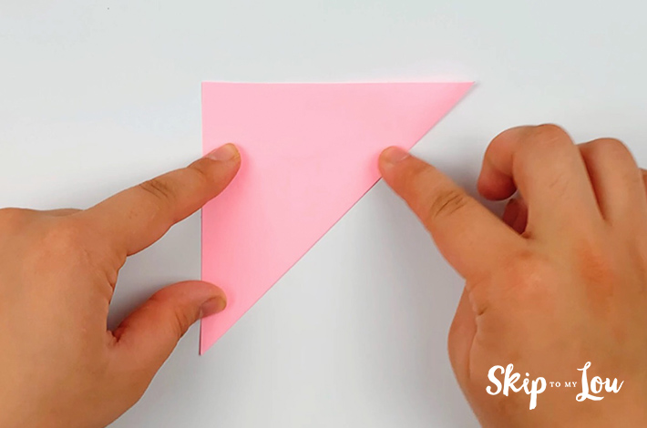 Two hands folding the paper in half into a triangular shape