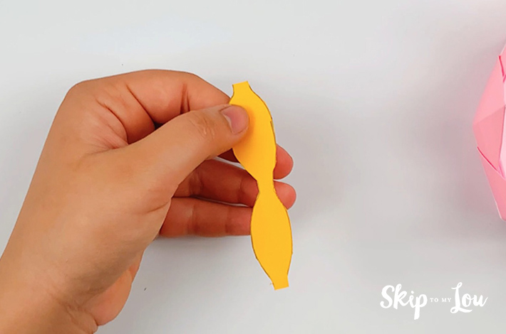 Twho hands holding the cut out shape from the rectangular piece of paper.