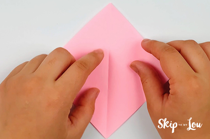 Two hand unfolding the paper with the points of one square pointing to the top.