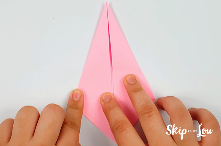 Two hands folding the left hand side of the paper towards the originally folded center line.