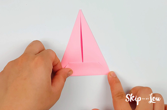 Two hand folding the paper from the bottom to form a straight fold.