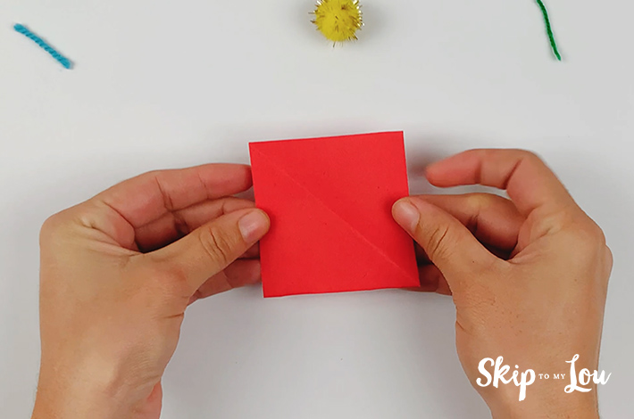 Two hands holding a red square piece of paper.