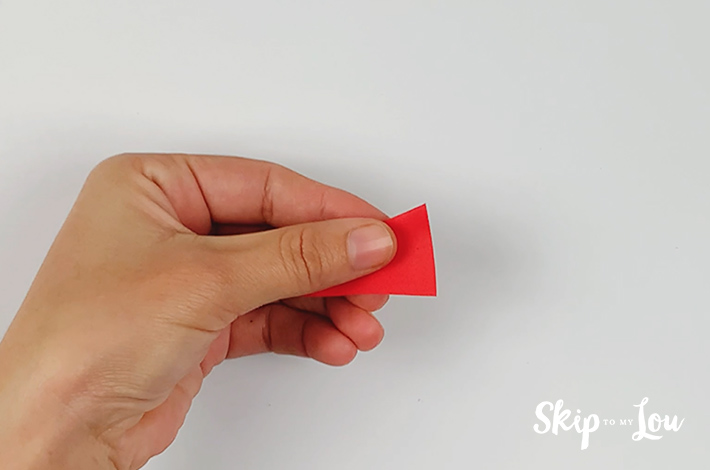 A hand holding the paper left after the back end of the triangle has been cut off.