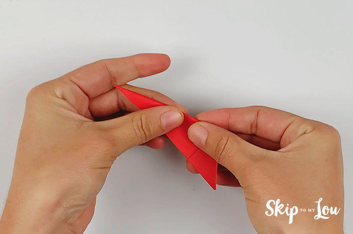Two hands making the first origami folds for a paper petal.