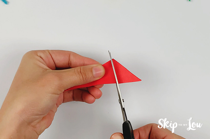 A pair of scissors cutting off the end of the triangle after the fold has been made.