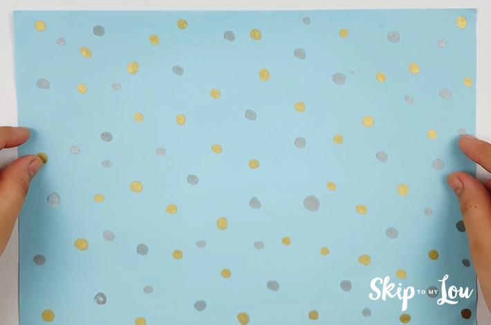 Two hands holding a square piece of wrapping paper.