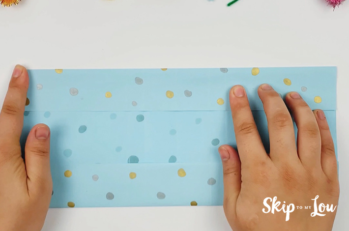 Two hands folding a bottom and top flap on the opened rectangular paper.