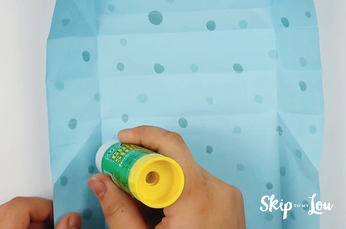 A hand applying glue to the unfolded paper.