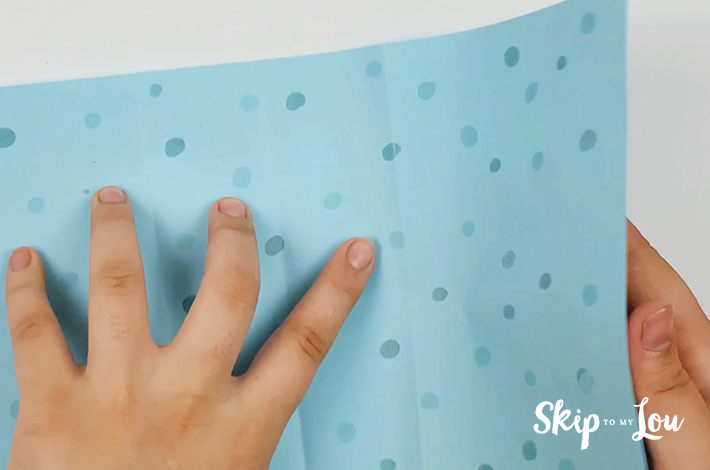 Two hands opening the paper to its full rectangular width.