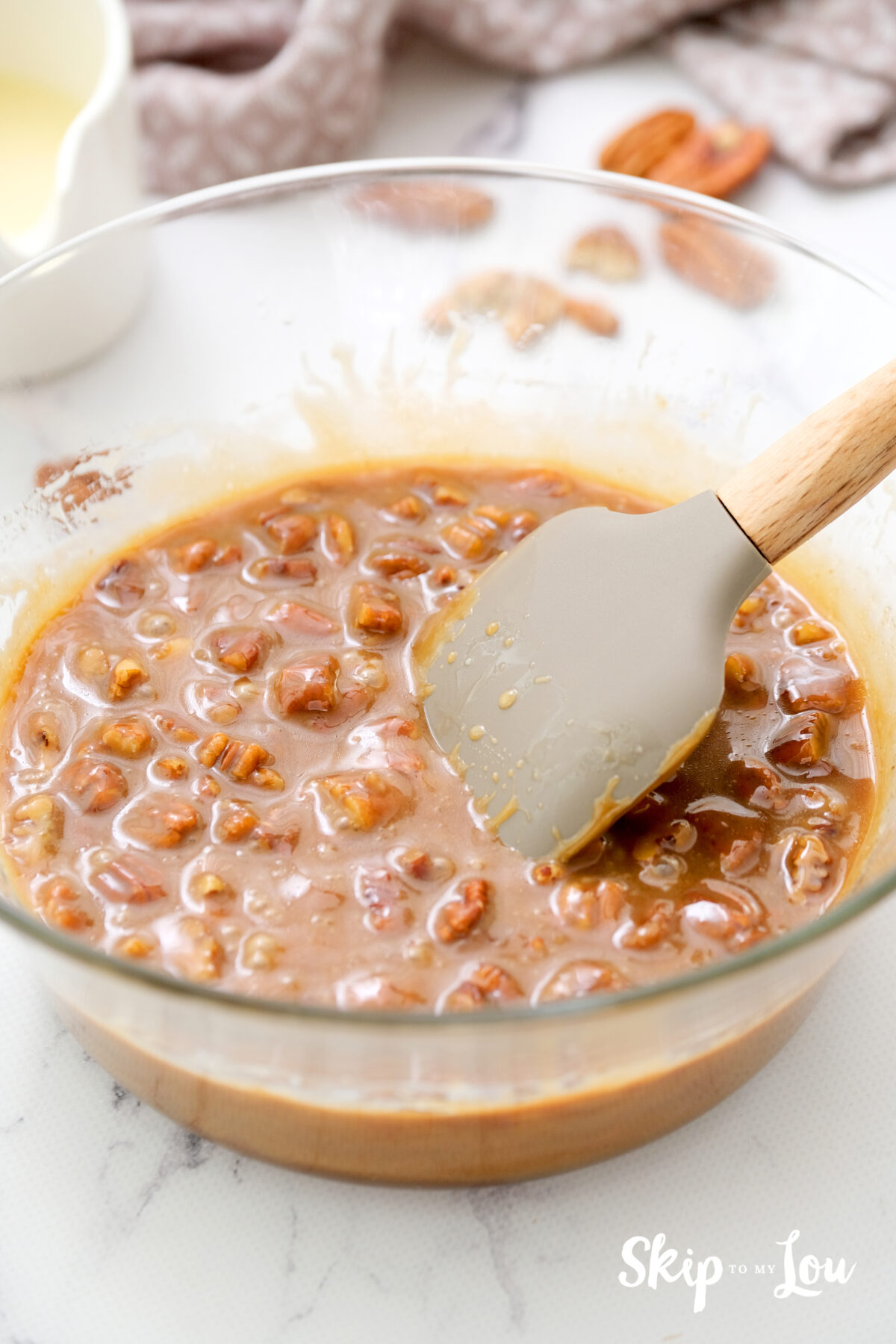 A bowl filled with pecans, caramel sauce and evaporated milk which are thoroughly mixed through.