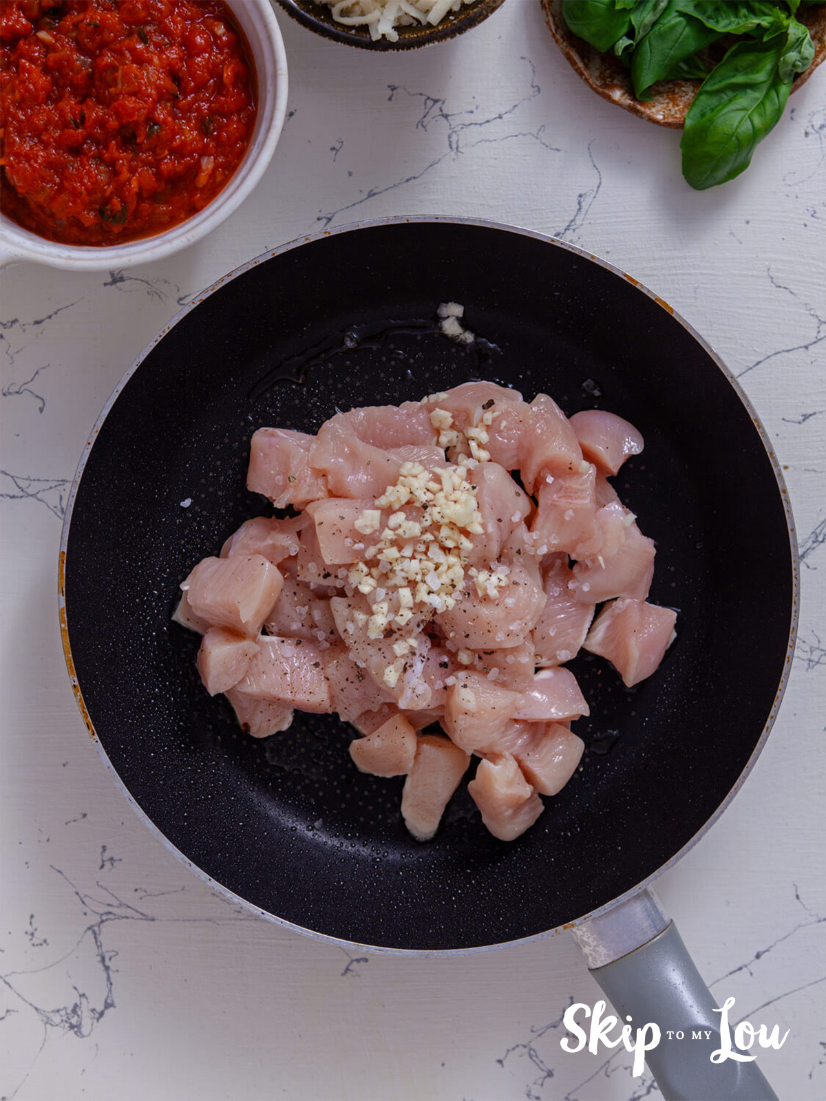 A skillet with cubed chicken, salt, pepper and garlic.