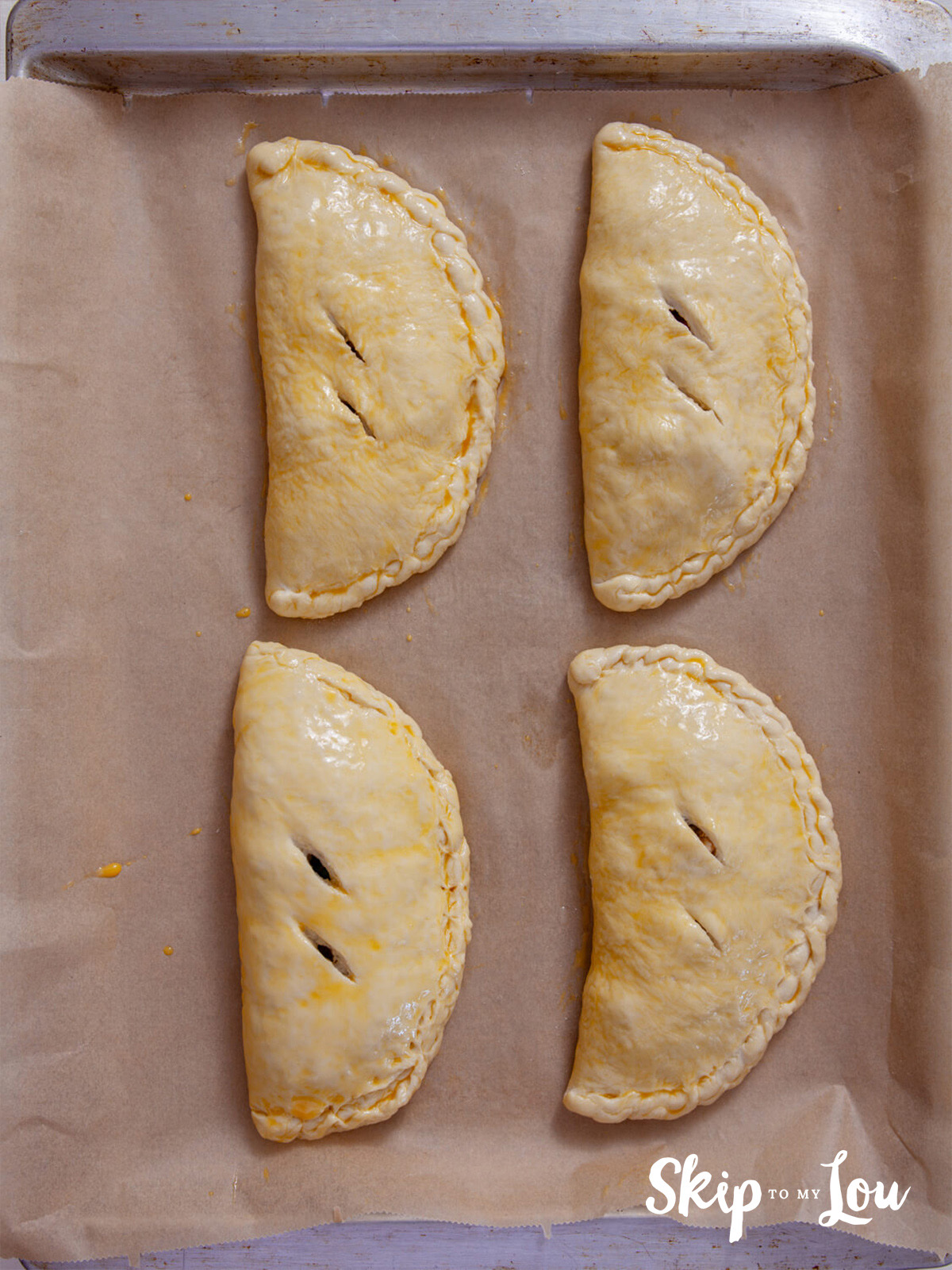 Calzones waiting to go in the oven after air holes are cut in them and they are brushed with beaten egg.