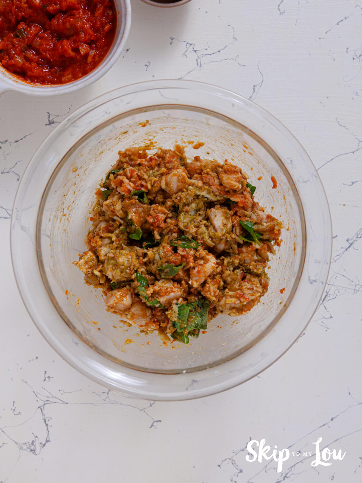 A large mixing bowl containing the cooked chicken, 1/4 cup of marinara sauce, pesto, mozzarella, parmesan, fresh basil and salt and pepper all thoroughly mixed through.