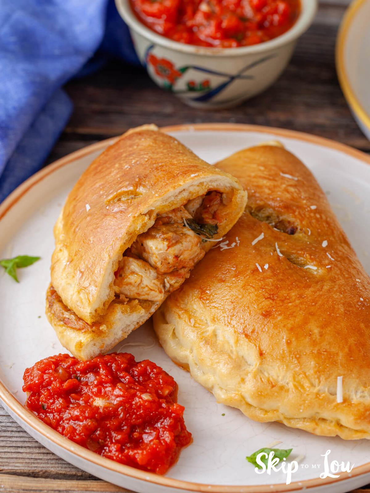 Chicken and peston calzone sitting on a white plate with a tomato sauce from a recipe from Skip to my Lou.