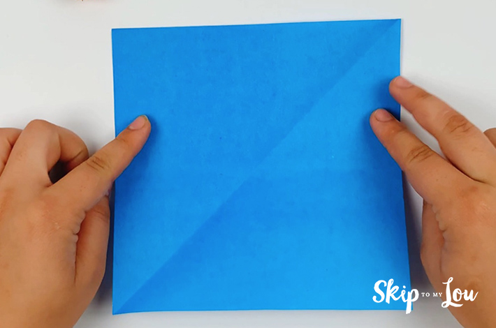 Two hands holding a blue square piece of paper.