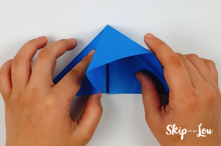 Two hands folding the paper inwards into a smaller triangle.