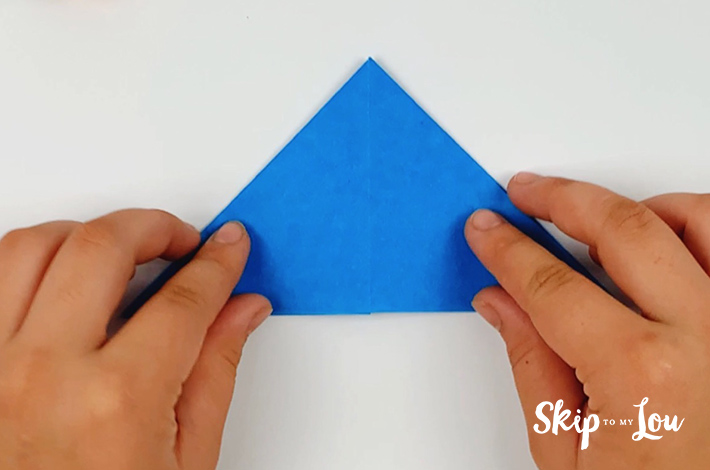 Two hands holding a smaller triangle folded from the square piece of paper.