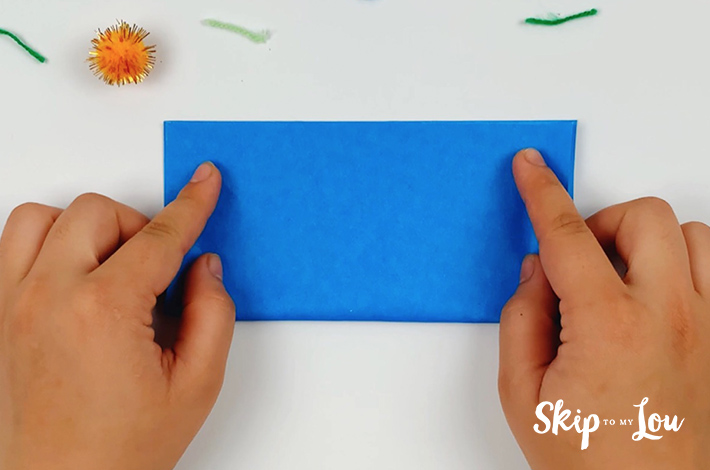 Two hands folding the blue paper in half.
