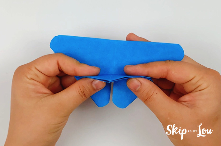 Two hands folding the bottom section of the triangle backwards towards the longer point.