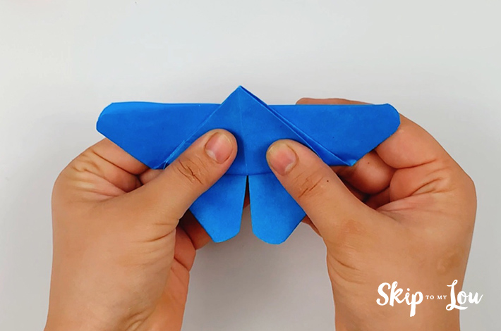 Two hands folding the bottom section of the triangle backwards towards the longer point with the point just going over the edge. 