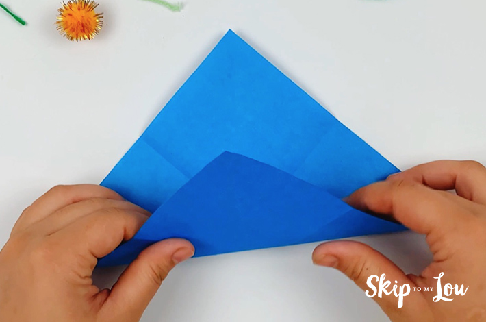 Two hands turning the paper 45 degrees and folding the bottom edge towards the top edge.