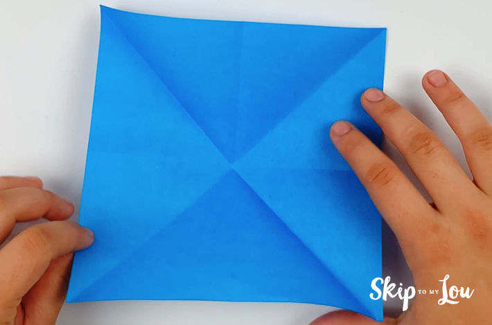 Two hands opening the paper out to the original square shape.