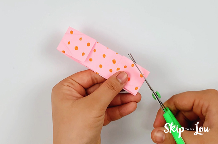 Two hands using a scissors to cut of all the corners at a 45 degree angle.
