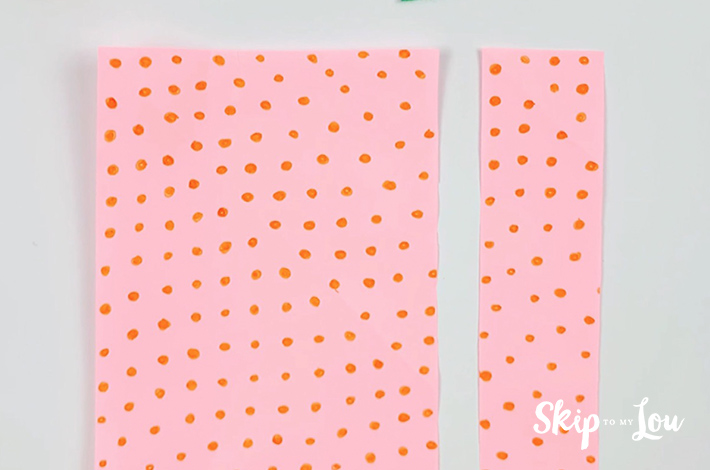 Two pieces of pink paper with orange dots. The second piece of paper has been cut along the fold made earlier.