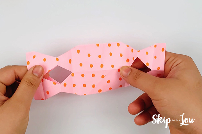 Two hands opening the folded paper to form a box shape.
