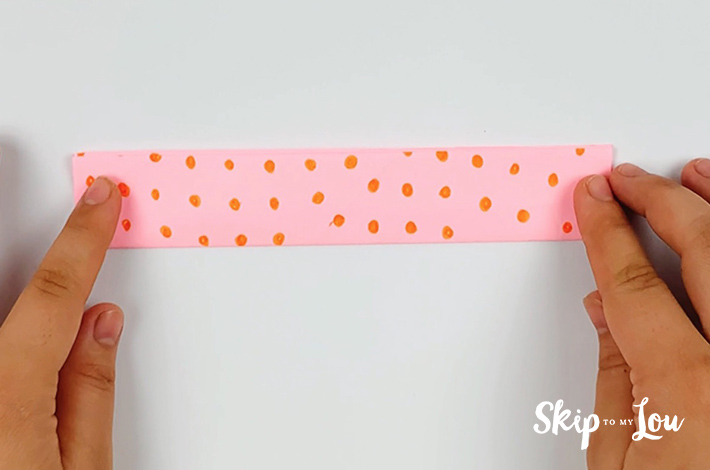 Two hands folding the of pink paper with orange dots in half in half again.
