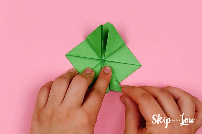 Two hands foldin gthe bottom right hand section of the diamond flap in half at a 45 degree angle. 