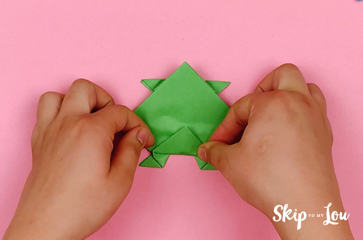 Two hands folding the bottom triangle upwards once the paper has been flipped over. 
