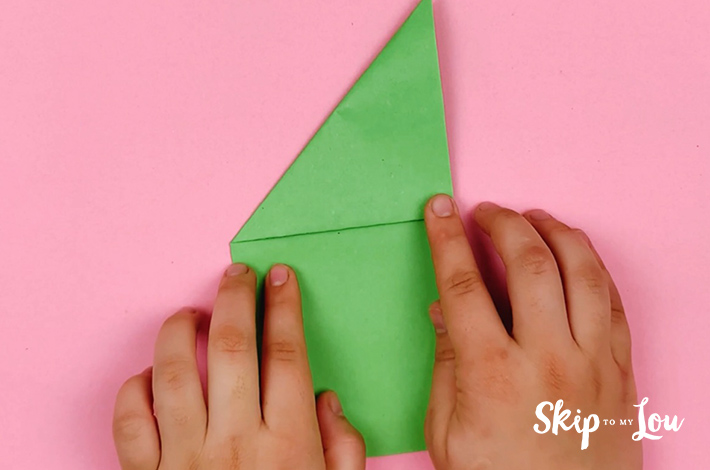 Two hands folding the top left corner along the visible crease line. 