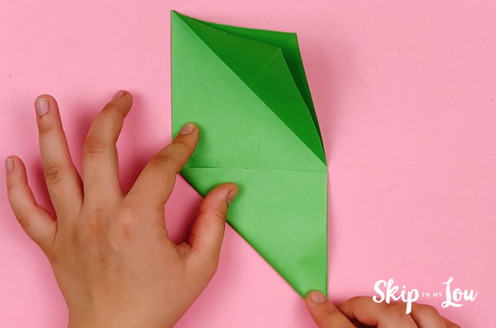Two hands folding the bottom left corner along the visible crease line. 