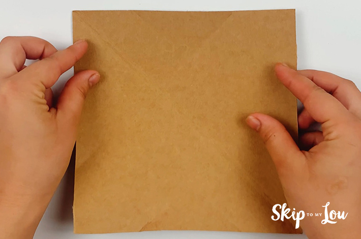 Two hands holding a brown rectangular piece of sturdy paper.
