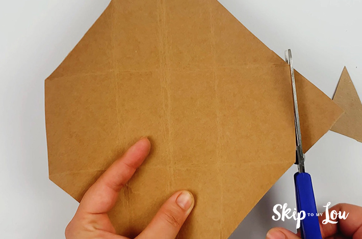 A pair of hands usings a scissors to cut off the right side and left side triangle along the folded lines. 